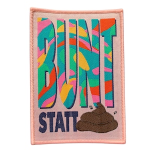 Könnte beinhalten: Ein rosa Stoff-Patch mit dem Text "BUNT STAT" in blauer Schrift. Das "BUNT" ist in einem bunten, abstrakten, wirbelnden Muster. Ein brauner Cartoon-Kacke befindet sich unter dem Text.
