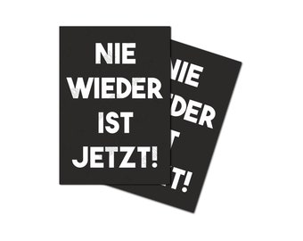 Könnte beinhalten: Zwei schwarze Karten mit weißem Text, der "NIE WIEDER IST JETZT!" lautet. Die Karten liegen übereinander, wobei die obere Karte leicht nach rechts versetzt ist.