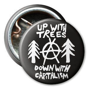 Könnte beinhalten: Schwarz-weißer Knopf mit dem Text "Up with Trees Down with Capitalism" und einem Anarchiesymbol. Auf jeder Seite des Anarchiesymbols befinden sich drei stilisierte Bäume.