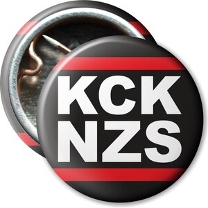Könnte beinhalten: Ein schwarzer und roter Knopf mit dem Text "KCK NZS" in weißen Buchstaben.