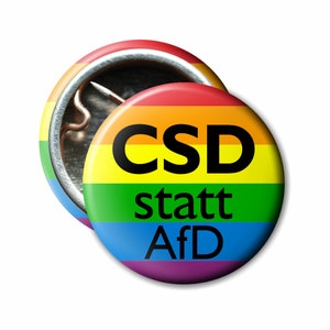 Könnte beinhalten: Ein regenbogenfarbener Knopf mit dem Text "CSD statt AfD" in schwarzen Buchstaben.