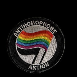 Könnte beinhalten: Ein gestickter schwarzer und weißer Aufnäher mit einer Regenbogenflagge und dem Text "Antihomophobe Aktion".