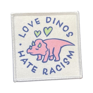 Könnte beinhalten: Quadratischer Aufnäher mit weißem Hintergrund und genähtem Rand. Der Aufnäher zeigt einen rosa Triceratops-Dinosaurier mit blauen Umrissen, zwei grünen Herzen und dem Text "LOVE DINOS HATE RACISM" in Blau, kreisförmig angeordnet.