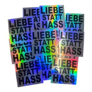 Könnte beinhalten: Eine Ansammlung quadratischer Aufkleber mit einer holografischen, regenbogenfarbenen Oberfläche. Jeder Aufkleber zeigt den fetten, schwarzen, serifenlosen Text "LIEBE STATT HASS" in drei Zeilen, was einen lebendigen und reflektierenden Effekt erzeugt.