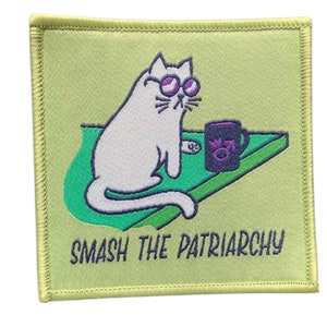 Könnte beinhalten: Ein grüner und weißer gestickter Aufnäher mit einer weißen Katze, die eine Sonnenbrille trägt und eine lila Tasse hält. Der Text "SMASH THE PATRIARCHY" befindet sich unter der Katze.