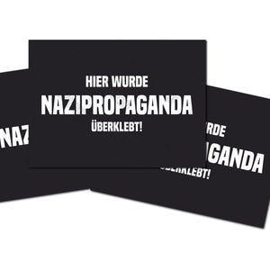 Könnte beinhalten: Drei schwarze Karten mit weißem Text. Die mittlere Karte lautet "HIER WURDE NAZIPROPAGANDA ÜBERKLEBT!". Die anderen Karten zeigen Teiltexte. Die Karten sind auf weißem Hintergrund angeordnet.