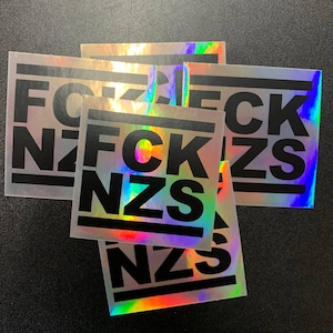 Könnte beinhalten: Vier schimmernde Aufkleber mit dem Text "FCK NZS" in schwarzen Buchstaben. Die Aufkleber sind holografisch und haben einen Regenbogeneffekt.