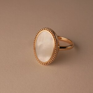 May include: A gold ring with a white oval-shaped stone set in a beaded bezel.