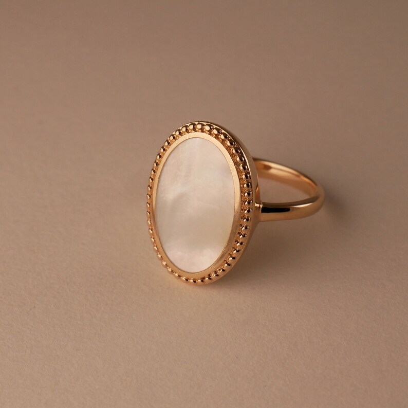 May include: A gold ring with a white oval-shaped stone set in a beaded bezel.
