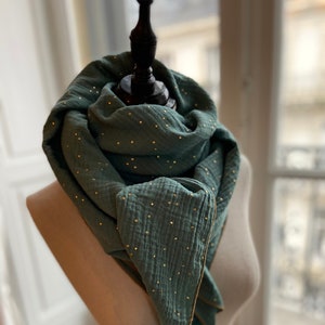 Peut inclure: Écharpe de couleur teal avec des détails dorés, présentée sur un mannequin. Le tissu est texturé et bordé d'or. Les embellissements dorés sont dispersés sur toute la surface. Un accessoire de mode élégant et polyvalent.