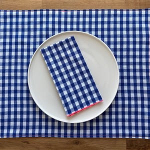 Peut inclure: Une assiette blanche avec une serviette en vichy bleu et blanc posée dessus. L'assiette est posée sur une nappe en vichy bleu et blanc.