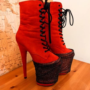 May include: A pair of red suede platform boots with black laces and a black glitter platform. The boots have a high heel and a pointed toe.