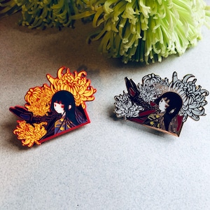May include: Two enamel pins featuring a woman with black hair and a red and gold kimono. The woman is surrounded by yellow and white chrysanthemums. The pins are set against a white background.