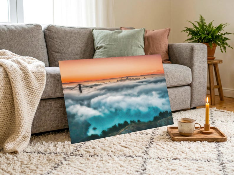 May include: A rectangular wall art print featuring a landscape photograph of the Golden Gate Bridge partially obscured by a thick layer of fog, with a vibrant orange sunset sky above and dark green hills visible in the foreground below the clouds.