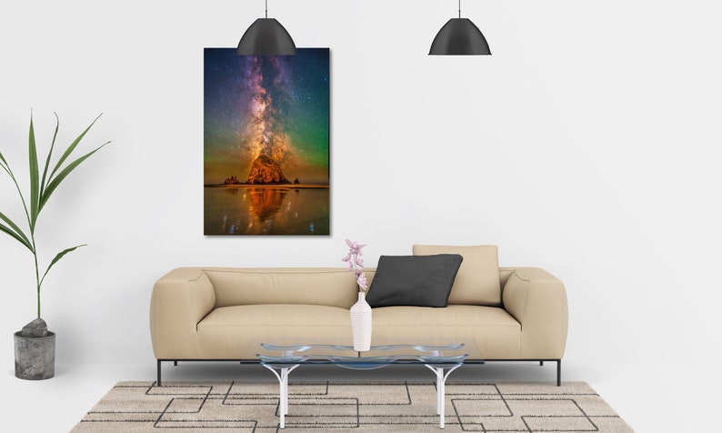 May include: A rectangular wall art print featuring a vibrant night sky with a glowing Milky Way galaxy above a large rock formation on a beach, with the scene reflected in the wet sand below, displayed in a modern living room setting.