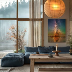 May include: A rectangular wall art print featuring a vibrant night sky with the Milky Way galaxy above a rocky coastal formation, displayed in a room with a blue sofa, a wooden table, and a large spherical paper pendant light fixture.