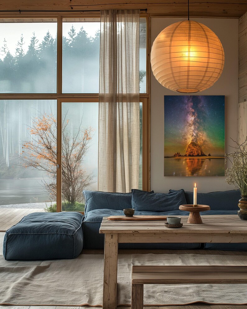 May include: A rectangular wall art print featuring a vibrant night sky with the Milky Way galaxy above a rocky coastal formation, displayed in a room with a blue sofa, a wooden table, and a large spherical paper pendant light fixture.