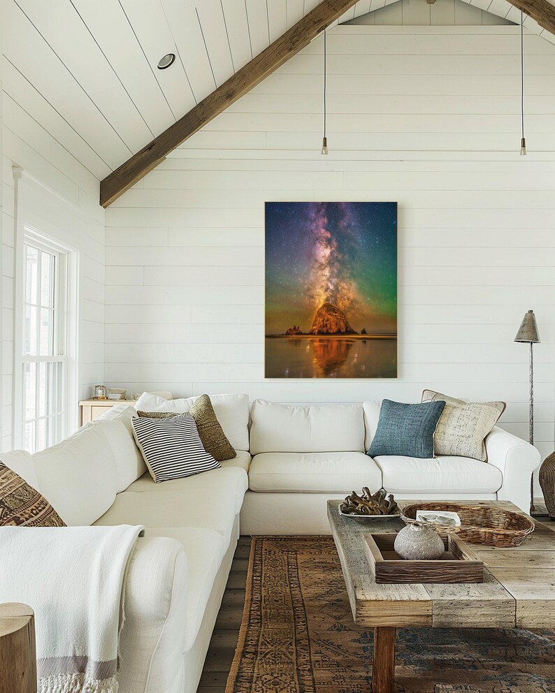 May include: A vertical wall art print featuring a night sky filled with a vibrant purple and orange Milky Way galaxy above a large, dark rock formation on a beach, with the scene reflected in the wet sand below the rock at the water's edge.