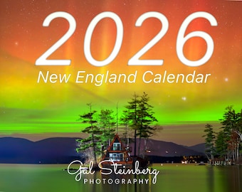 May include: A 2026 New England Calendar featuring a scenic landscape with a house on a small island, surrounded by water and trees. The sky displays vibrant colors of orange, yellow, and green, with the photographer's name at the bottom.