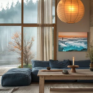 May include: A rectangular wall art print featuring a landscape of a bridge emerging from thick fog under a sunset sky, displayed in a living room with a blue sofa, a wooden table, a lit candle, and a large spherical paper pendant light.
