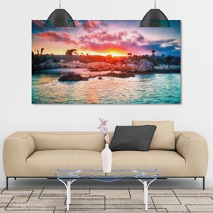 May include: A colourful sunset over a rocky coastline with turquoise water. The sky is a mix of pink, orange, and purple, with clouds reflecting in the water.