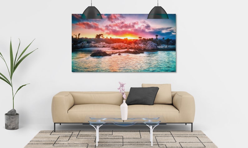 May include: A colourful sunset over a rocky coastline with turquoise water. The sky is a mix of pink, orange, and purple, with clouds reflecting in the water.