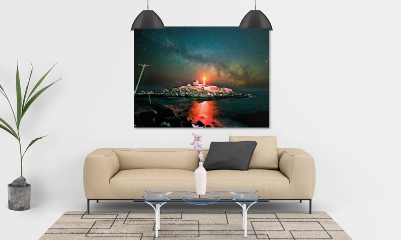 May include: A photograph of a lighthouse on a small island with the Milky Way visible in the night sky. The lighthouse is lit up and reflecting in the water.