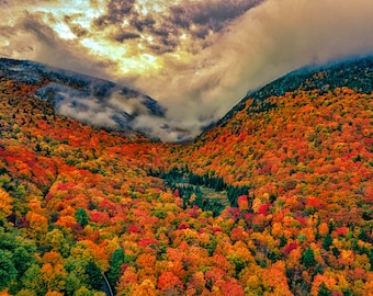 May include: Aerial view of a mountain valley covered in vibrant fall foliage. The trees are a mix of red, orange, yellow, and green. The valley is shrouded in mist, creating a dreamy atmosphere.