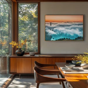 May include: A rectangular wall art print featuring a landscape of a bridge emerging from thick clouds at sunset, displayed in a thin frame. The scene shows a bridge tower and distant city skyline above a dense layer of fog with orange sky.
