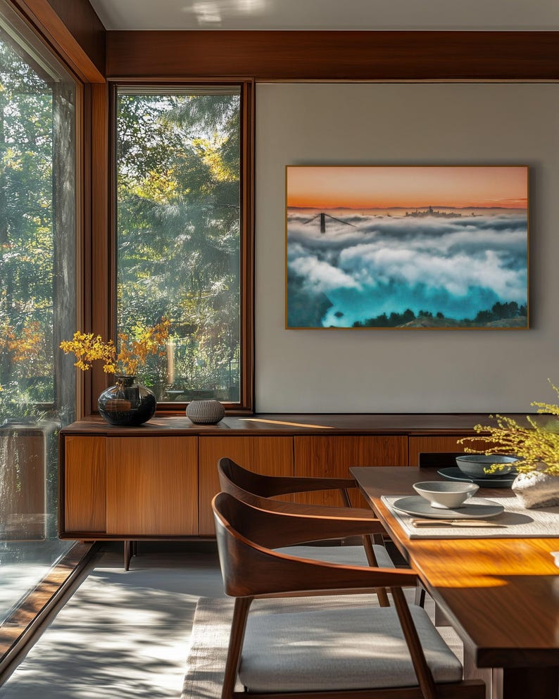 May include: A rectangular wall art print featuring a landscape of a bridge emerging from thick clouds at sunset, displayed in a thin frame. The scene shows a bridge tower and distant city skyline above a dense layer of fog with orange sky.