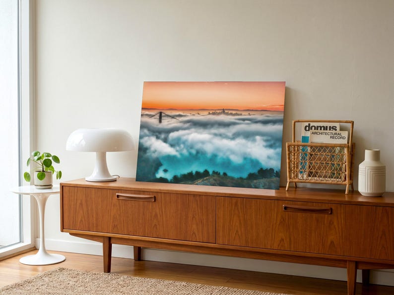 May include: A rectangular wall art print featuring a landscape photograph of the Golden Gate Bridge partially obscured by a thick layer of low-hanging clouds under a vibrant orange sunset sky, displayed as a standalone piece of home decor.
