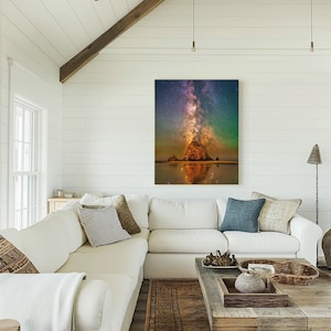 May include: A rectangular wall art print featuring a night sky filled with stars and a vibrant purple and orange nebula above a large rock formation on a beach, with the scene reflected in the wet sand below the rock at the water's edge.