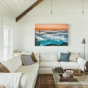 May include: A rectangular wall art print featuring a landscape view of the Golden Gate Bridge partially obscured by thick, low-hanging clouds under a vibrant orange sunset sky, with deep blue tones visible in the shadowed areas below the fog.