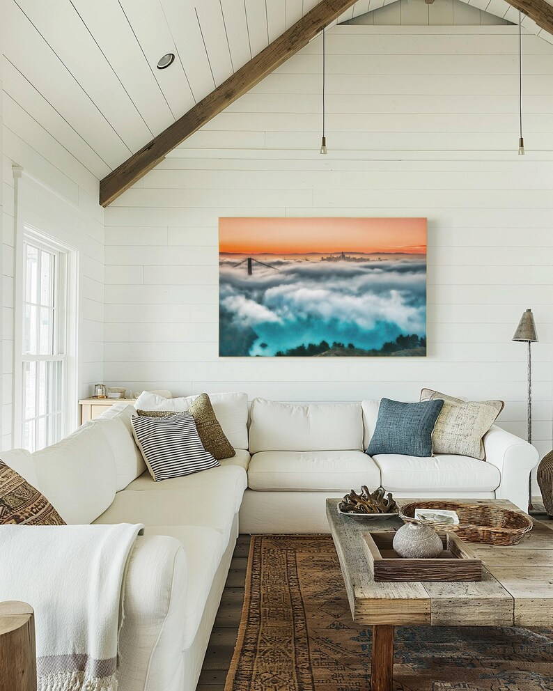 May include: A rectangular wall art print featuring a landscape view of the Golden Gate Bridge partially obscured by thick, low-hanging clouds under a vibrant orange sunset sky, with deep blue tones visible in the shadowed areas below the fog.