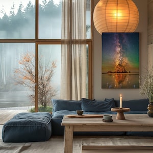 May include: A rectangular wall art print featuring a vibrant night sky with a glowing Milky Way galaxy above a large rock formation on a beach, with reflections on the wet sand, displayed in a room with a blue sofa and wooden furniture.