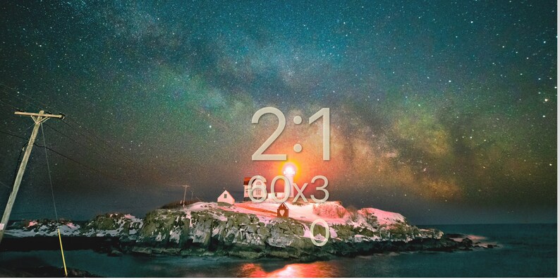 May include: A lighthouse on a rocky island with a starry night sky. The Milky Way is visible in the sky. The text "2:1 60x3 0" is visible in the image.