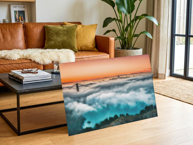 May include: A rectangular wall art print featuring a landscape photograph of the Golden Gate Bridge partially obscured by a thick layer of low-hanging fog, with a vibrant orange sunset sky above and dark green hills visible in the foreground.