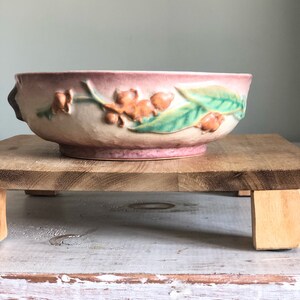 May include: A vintage ceramic planter with a pink glaze and a floral design. The planter features raised leaves and flowers in shades of green, brown, and orange.