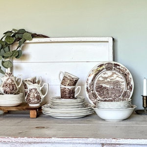 May include: A vintage brown and white patterned tea set with a creamer, sugar bowl, and cups. The set is arranged on a wooden table with a white background.