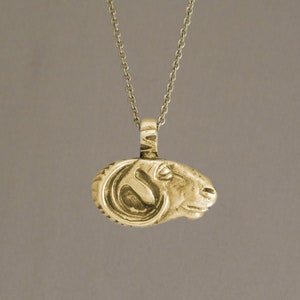 May include: A gold necklace with a pendant shaped like a ram's head.