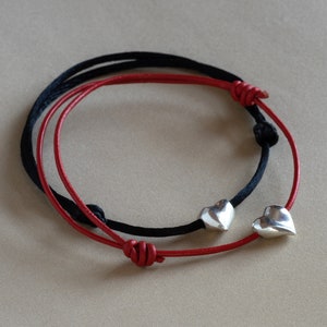 May include: Two friendship bracelets with heart charms. One bracelet is red and the other is black.