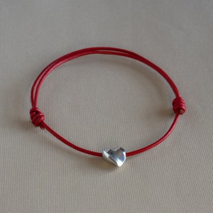 May include: A red leather bracelet with a silver heart charm.
