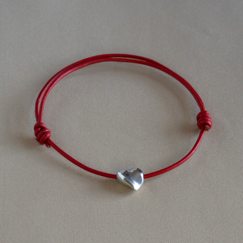 May include: A red leather bracelet with a silver heart charm.