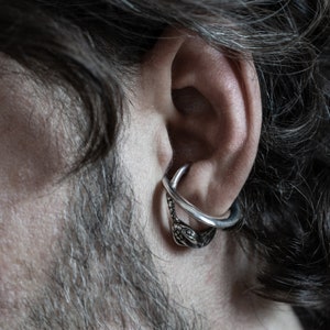 May include: A silver snake earring with a hoop design. The earring is worn in the upper cartilage of the ear.