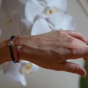 May include: Two bracelets with silver heart charms. One bracelet is red and the other is black.