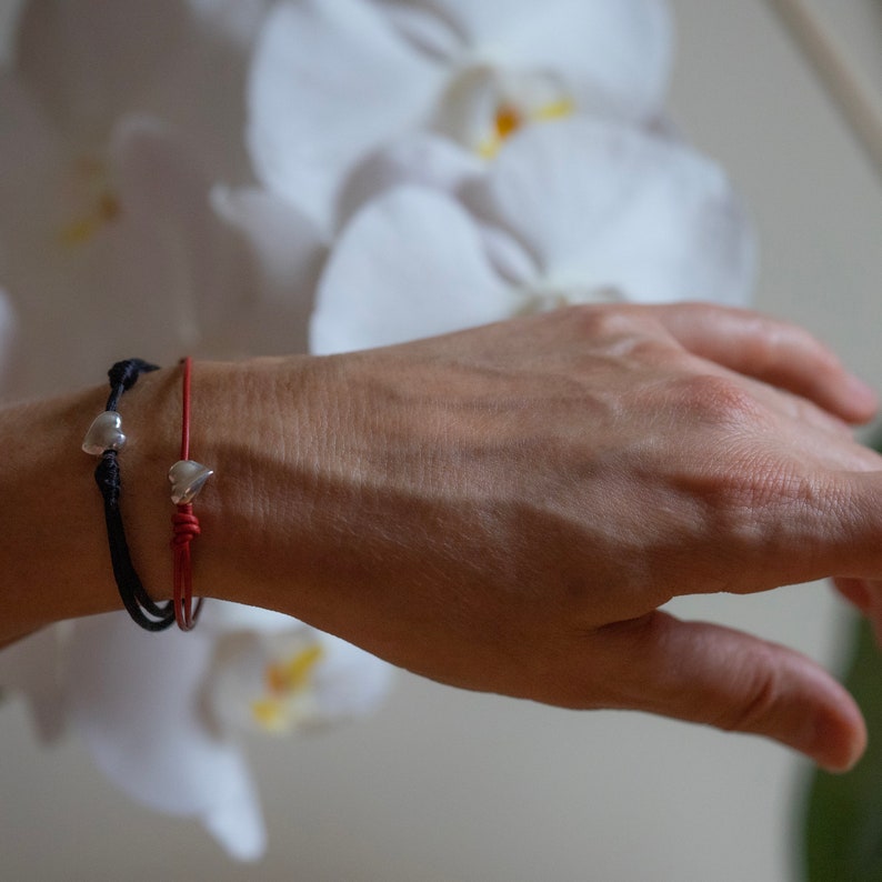 May include: Two bracelets with silver heart charms. One bracelet is red and the other is black.