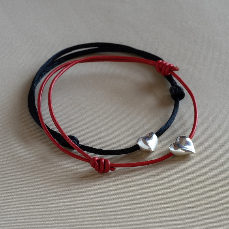 May include: Two friendship bracelets with heart charms. One bracelet is red and the other is black.