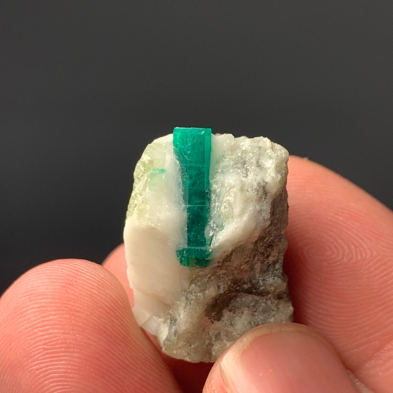 Puede incluir: Un peque&ntilde;o cristal de esmeralda verde incrustado en una matriz de roca blanca y gris.