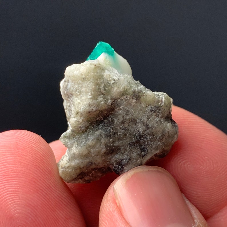 Puede incluir: Una peque&ntilde;a roca gris rugosa con un cristal de esmeralda verde brillante en la parte superior.