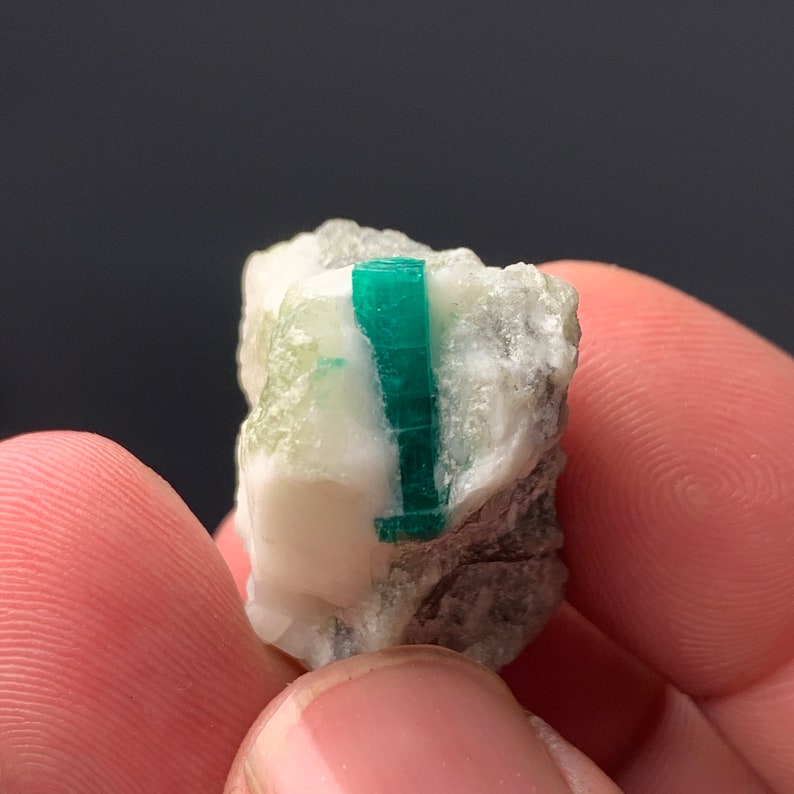Puede incluir: Un peque&ntilde;o cristal de esmeralda verde incrustado en una matriz de roca blanca y gris.